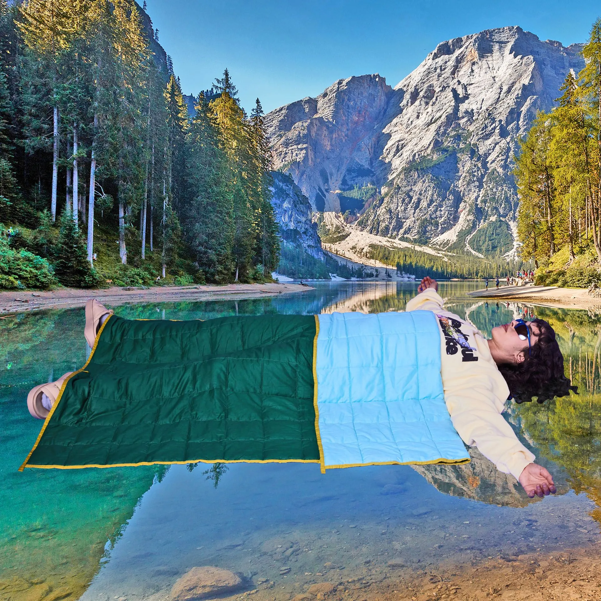 A person wearing Meaningful Existence clothes lies under a camping blanket super-imposed over a beautiful mountain scene.