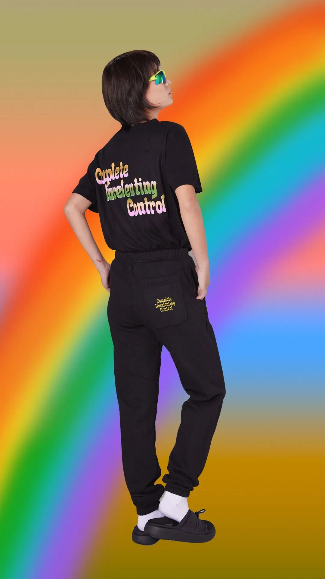 A model showing off a black Meaningful Existence sweatsuit over a rainbow background